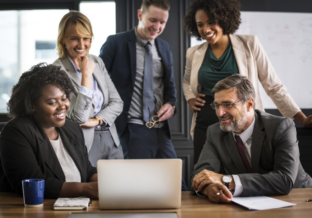 After Choosing SC: SC employees sitting around a table smiling, while looking at an email, and relieving board members from answering directly to community members.